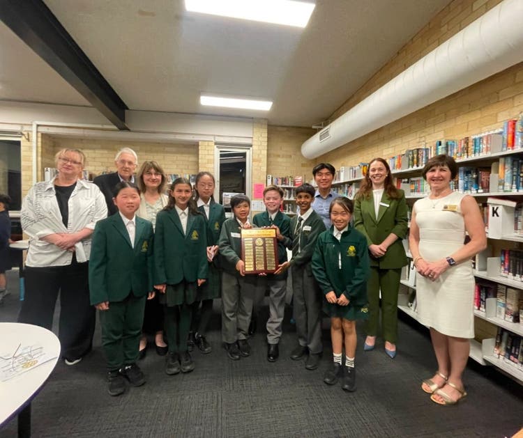 Debating team holding the winning trophy with a group of adults standing next to them.