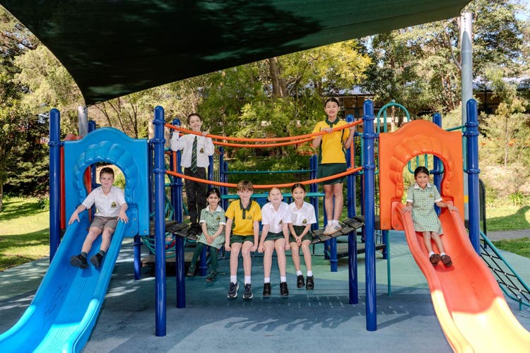 Students sitting on fixed playground equipment for a posed photo.