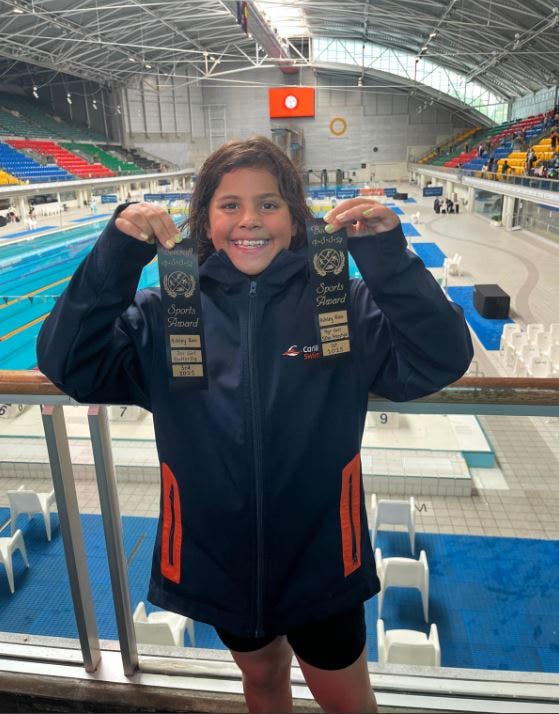 Student holding two swimming ribbons at the regional swimming championships