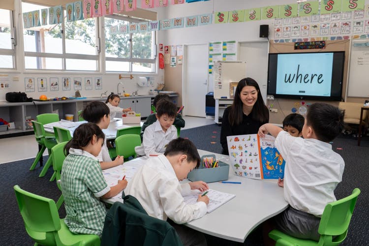 Group of Kindergarten students sitting at their desk with their teacher doing a handwriting lesson