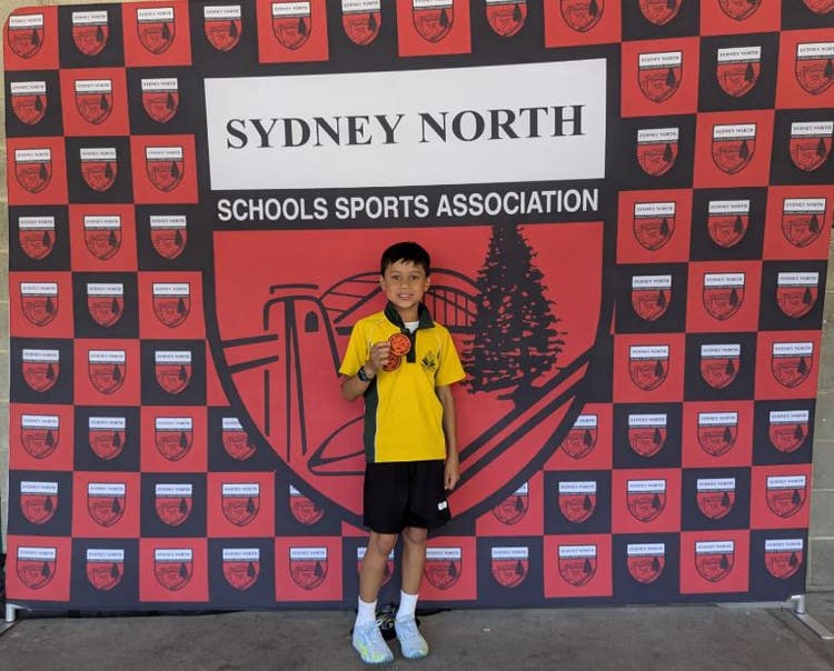 Student standing in front of Sydney North School Sport Association banner holding a patch.