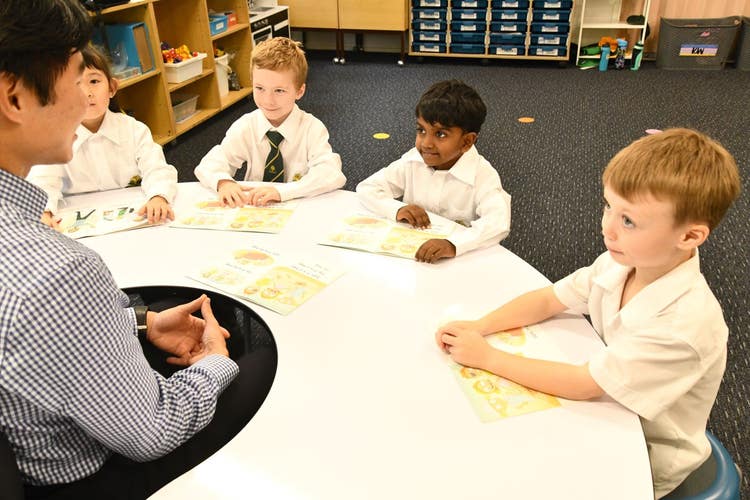 Fours students sitting around a table looking at their teacher reading a story together