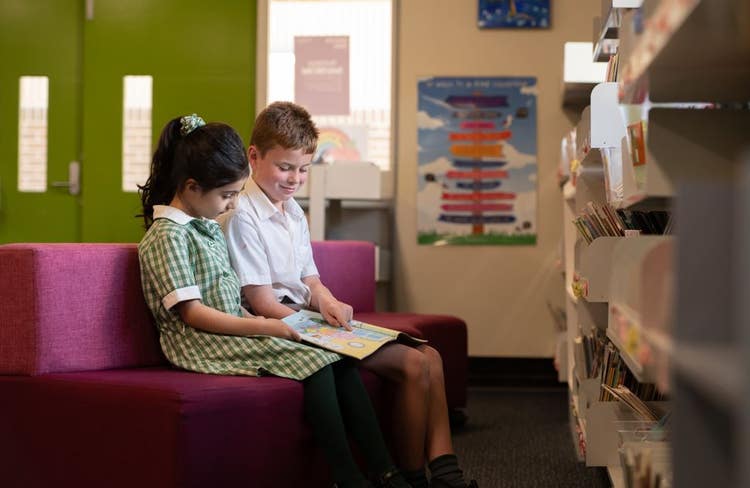 Two students sitting reading a book together in the library
