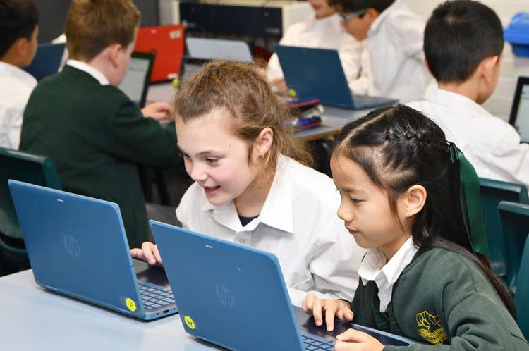 Two girls sitting side by side working on laptops