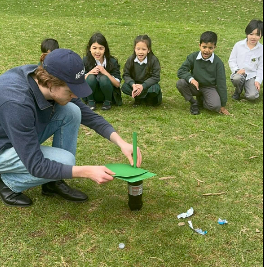Volunteer running a coke and mentos experiment on science day with students watching in the background