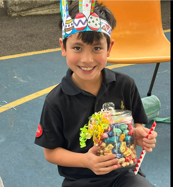 Child holding a glass jar of easter eggs. He is wearing an easter hat.