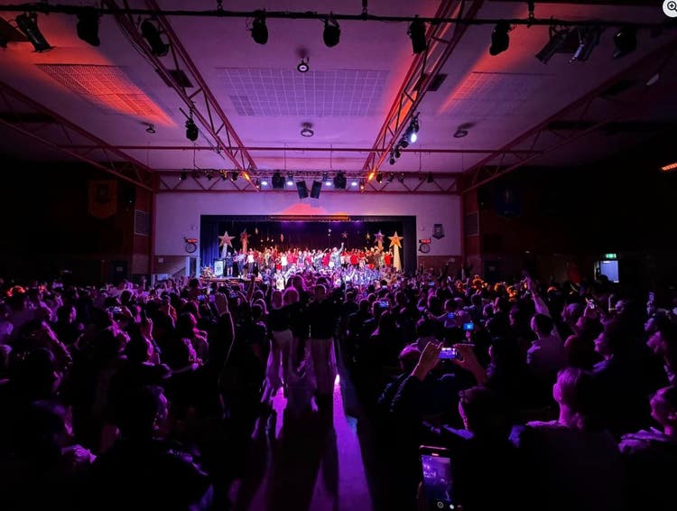 Hall filled with an audience and students performing on stage