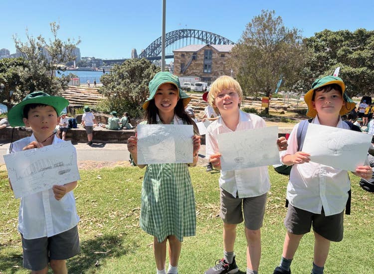 Four students posing for a photo in front of the Harbour Bridge holding their own sketch of the bridge.