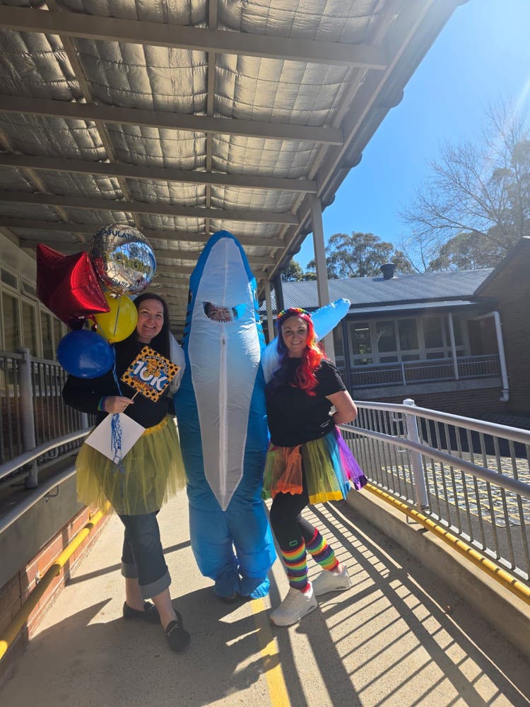 Two women in bright coloured skirts with a person in a shark costume in the middle